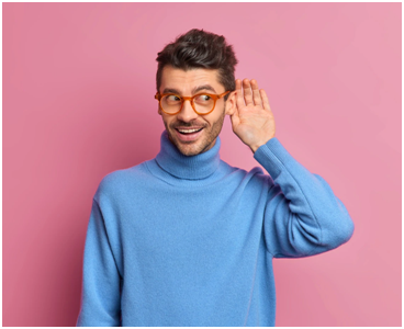 Homme avec des lunettes rouges sur fond rose porte sa main à l'oreille pour mieux écouter